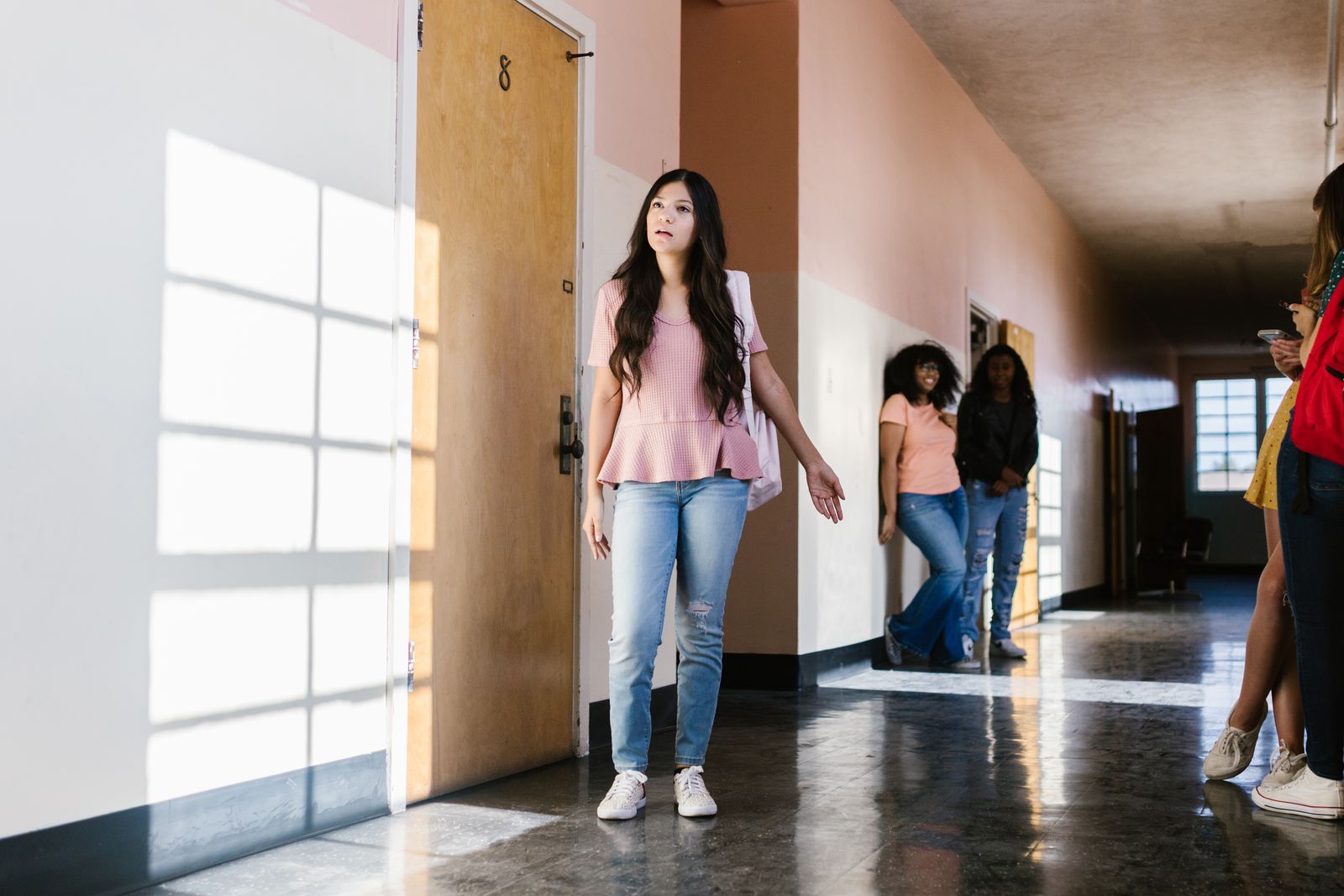 Teenage girl in school corridor looking thoughtful, surrounded by peers, captured in natural lighting.