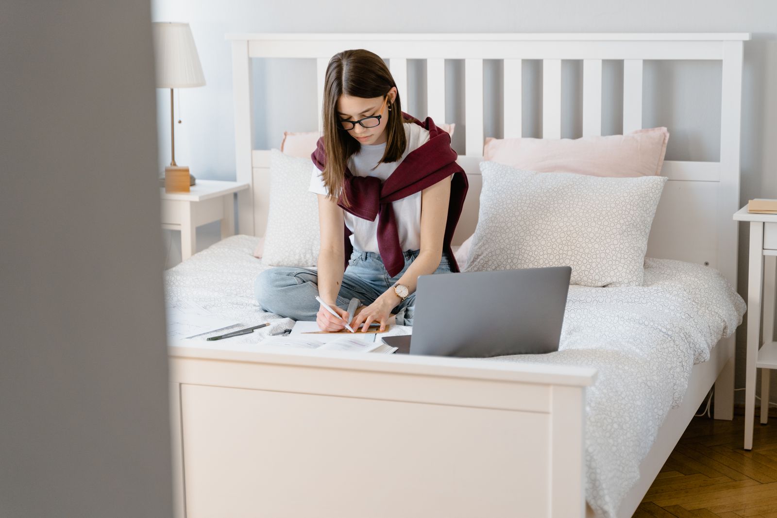 Teenage girl studying with laptop in a cozy bedroom setting.