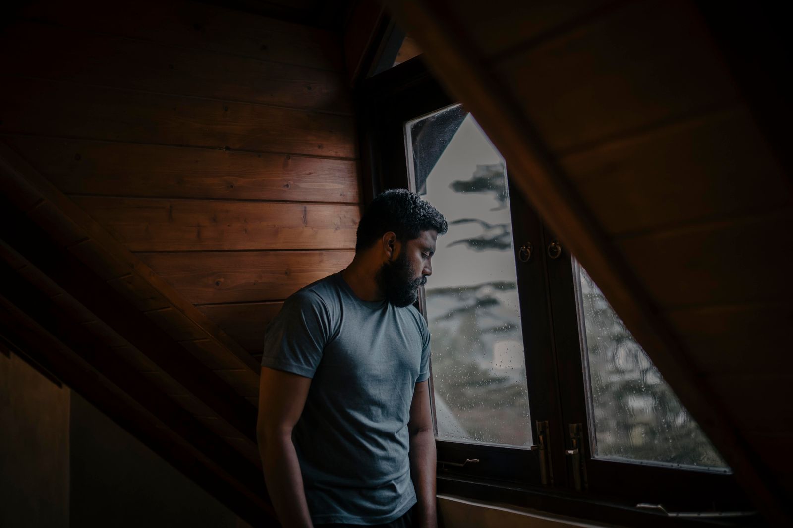A thoughtful man stands by a window, lost in contemplation, indoors in Sri Lanka.