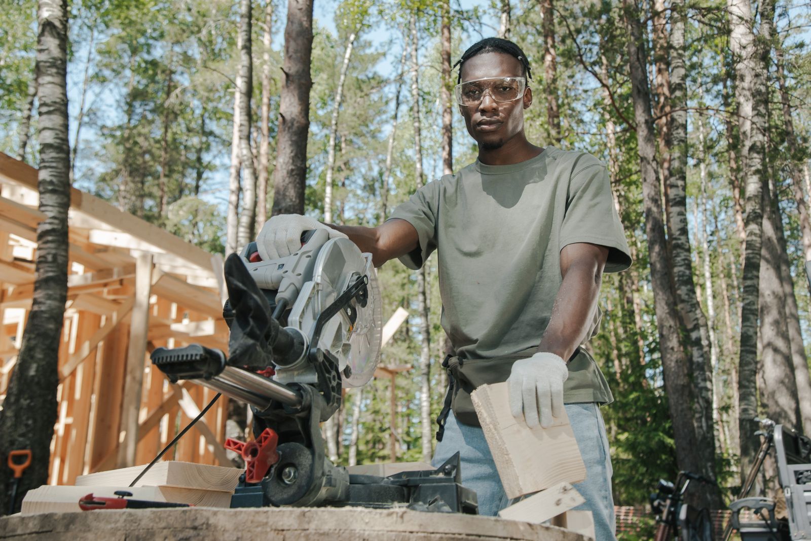 African American carpenter using a circular saw at a construction site in a forest.