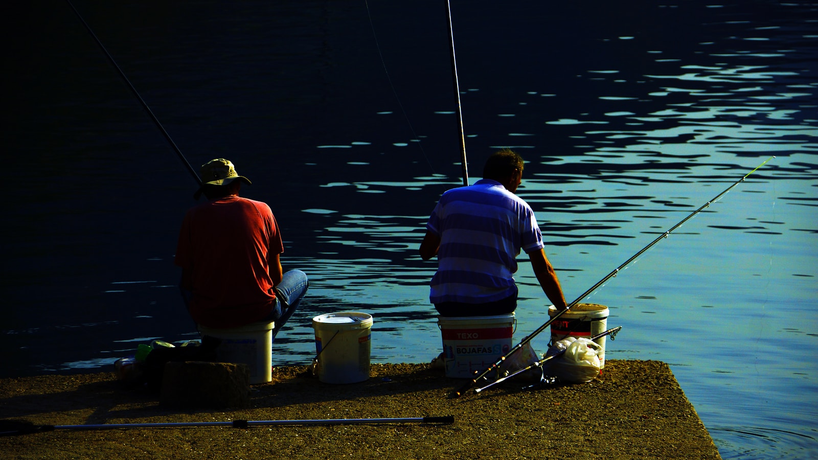 a couple of men sitting next to a body of water