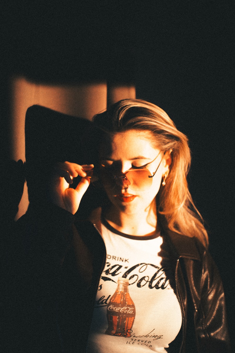 Woman in sunglasses adjusts them against dark background