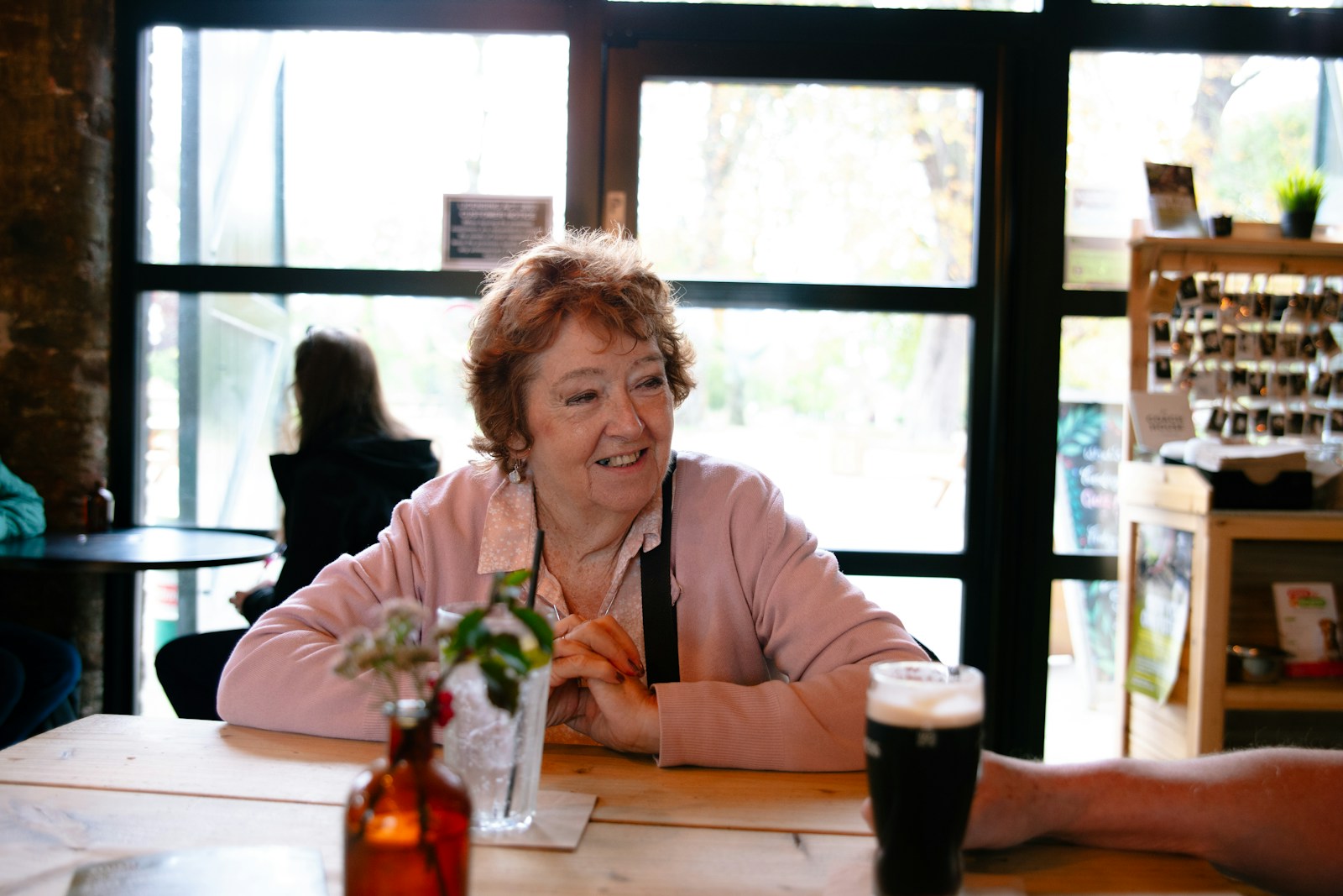 Elderly woman smiling at a table with beer.