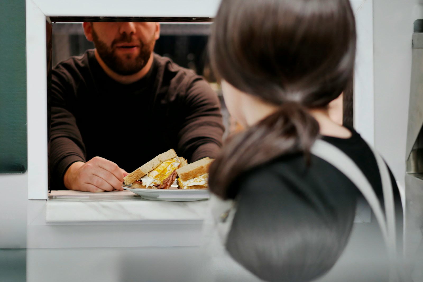 Man hands sandwich through a window to customer.
