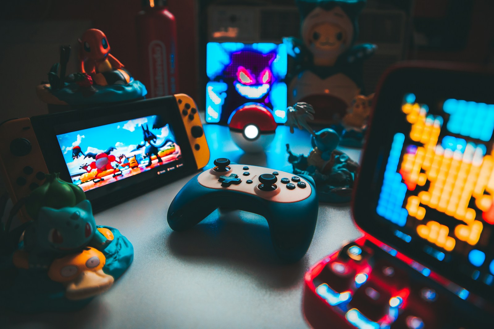 A handheld game console and controller surrounded by various character figurines on a desk
