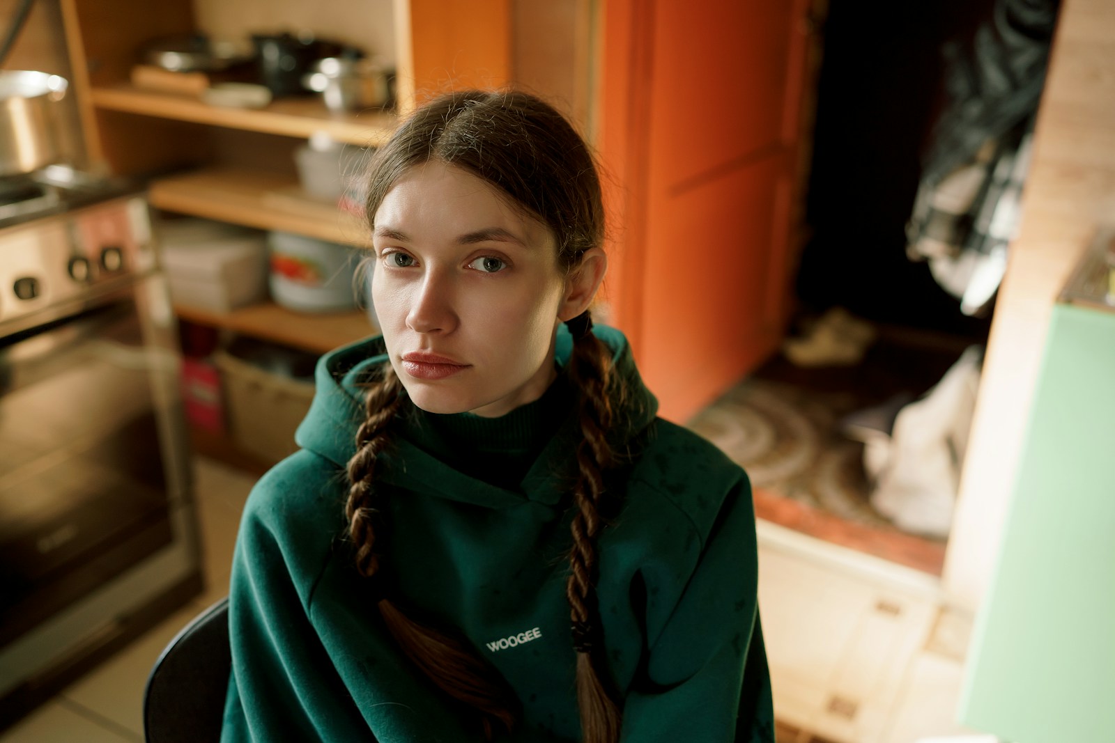 A young woman with braids wearing a green hoodie indoors.