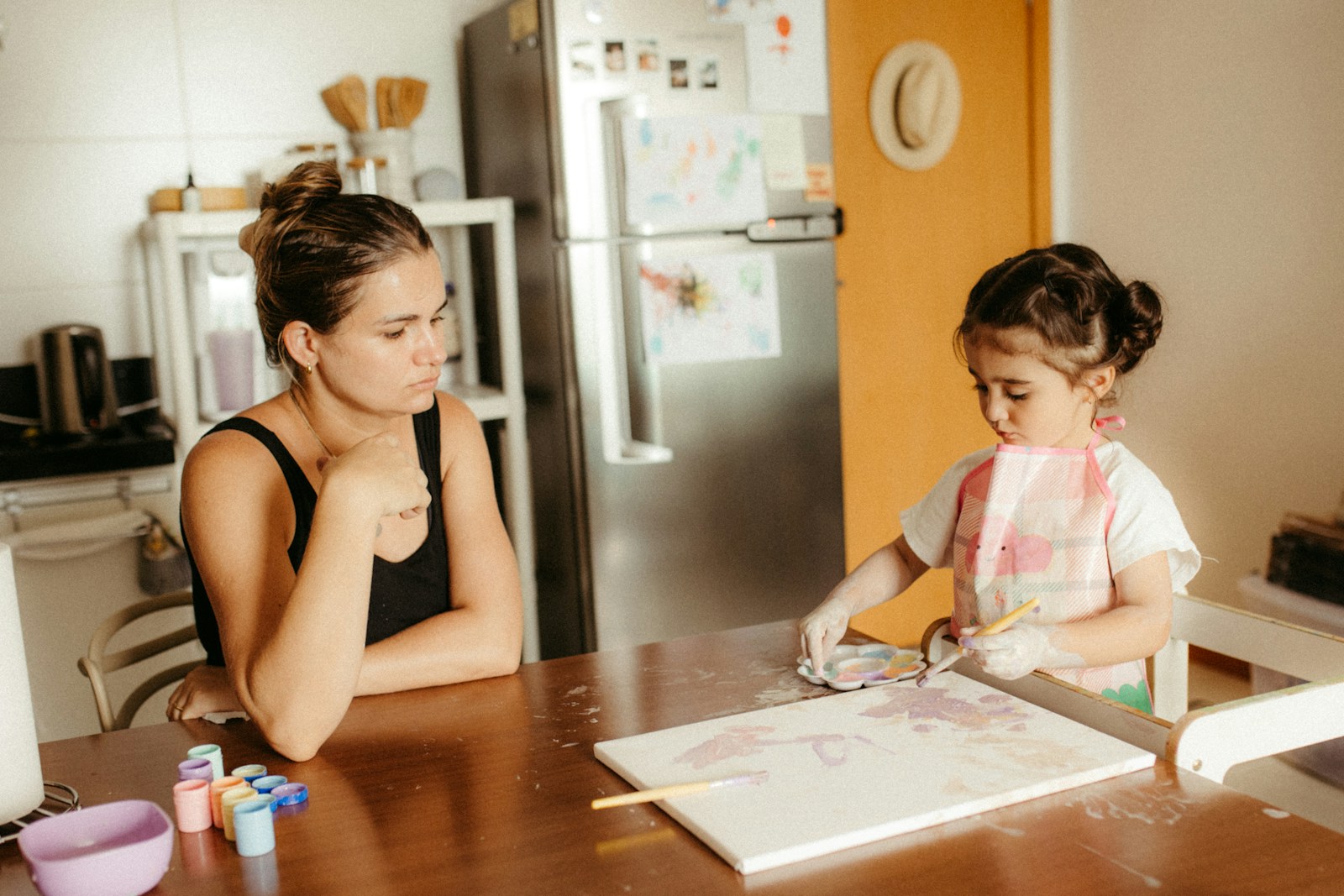 Mother watches daughter paint at kitchen table.