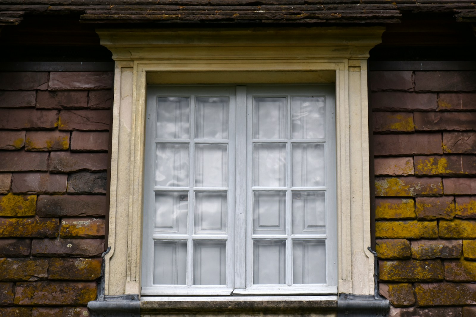 A closed window with white curtains on a brick wall