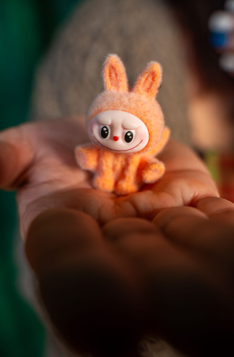 A cute, orange toy bunny rests in a person's palm, showcasing its small size and charm.