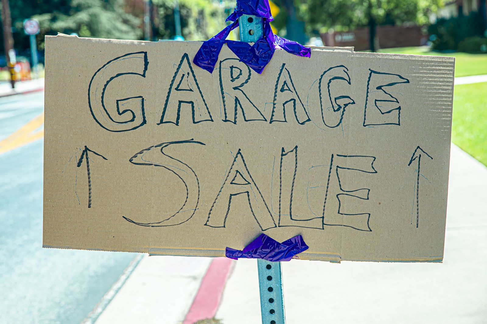 A handwritten garage sale sign taped on cardboard, displayed outdoors.