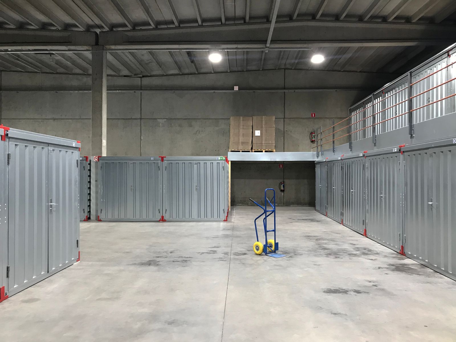 Modern warehouse interior with metal storage units and a blue hand truck on the concrete floor.