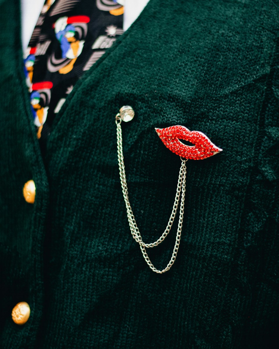 A man wearing a green suit with a red lips pin on his lapel
