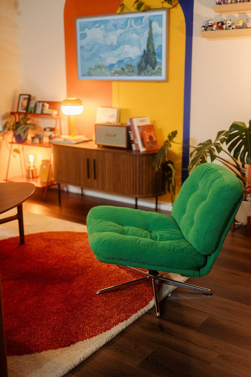 A green corduroy armchair on a round red rug in a colorful living room