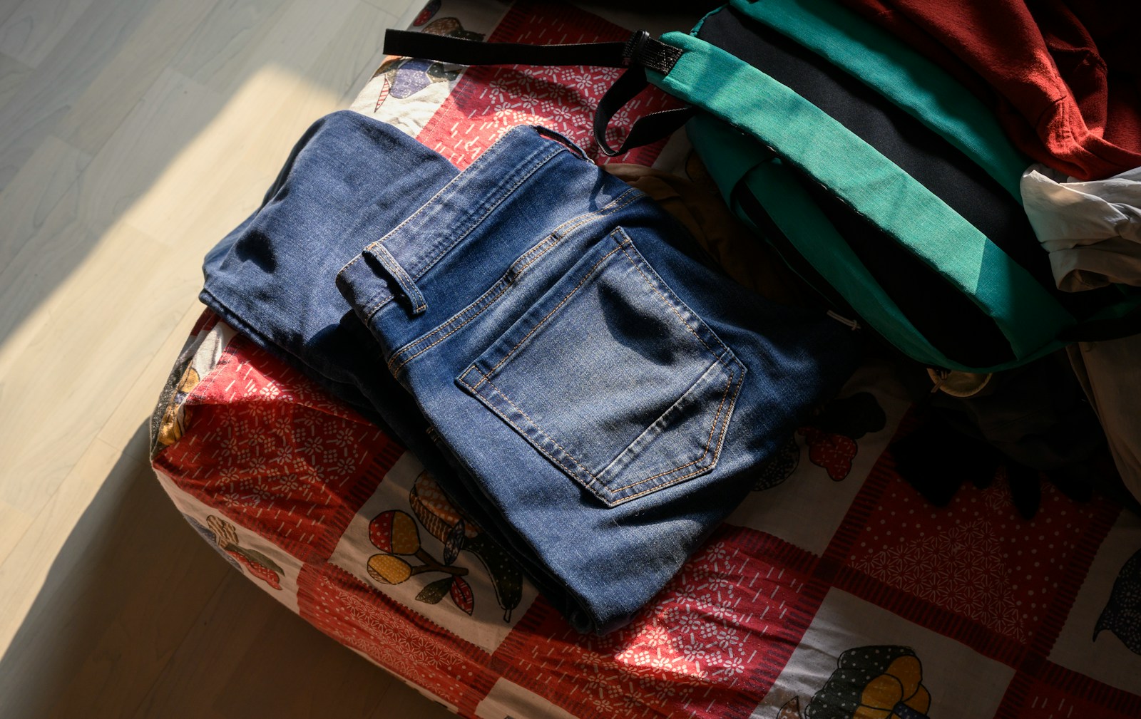 Blue jeans and a green bag on a patterned bed