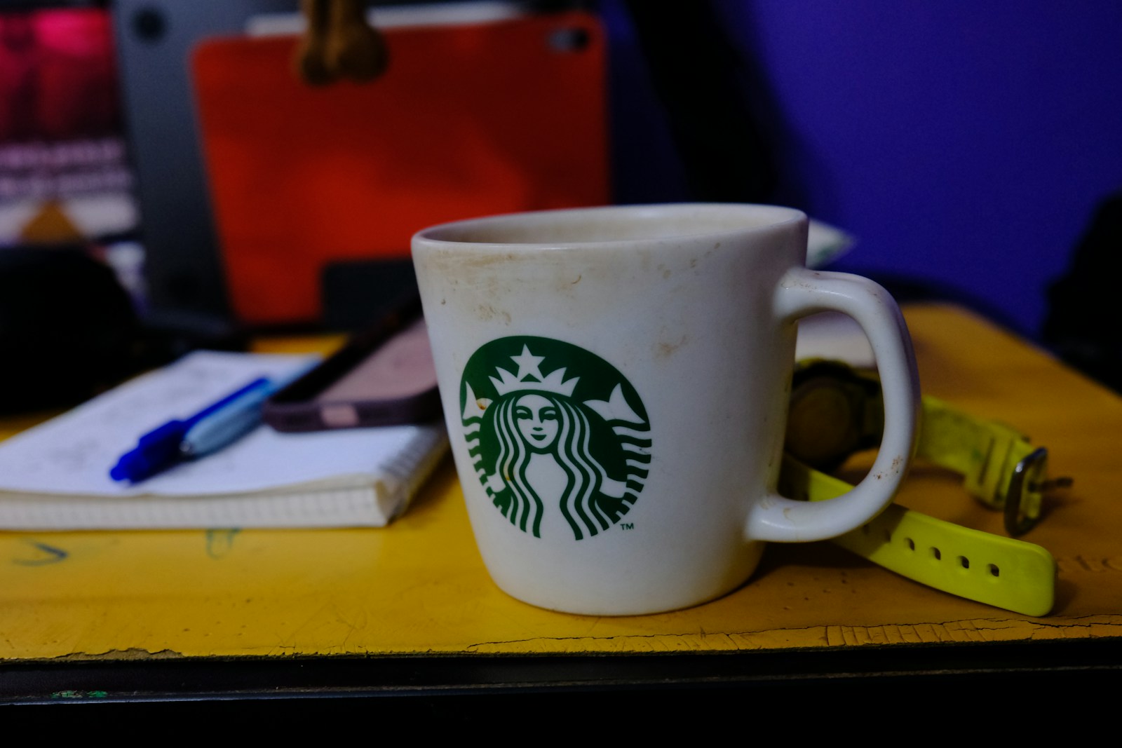 A white coffee mug with a green logo on a yellow desk surface
