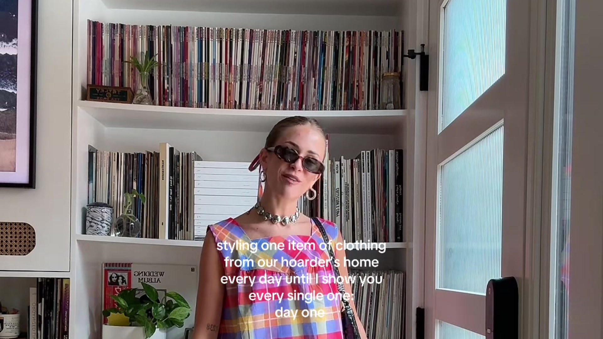 Sydney Lima in a plaid dress from the hoarder house she bought sight unseen, standing in front of shelves of vinyl records