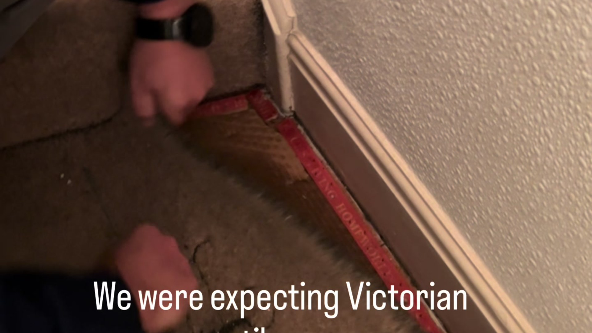 Homeowner pulling up old carpet at the edge of a room in a Victorian house, expecting original tile underneath