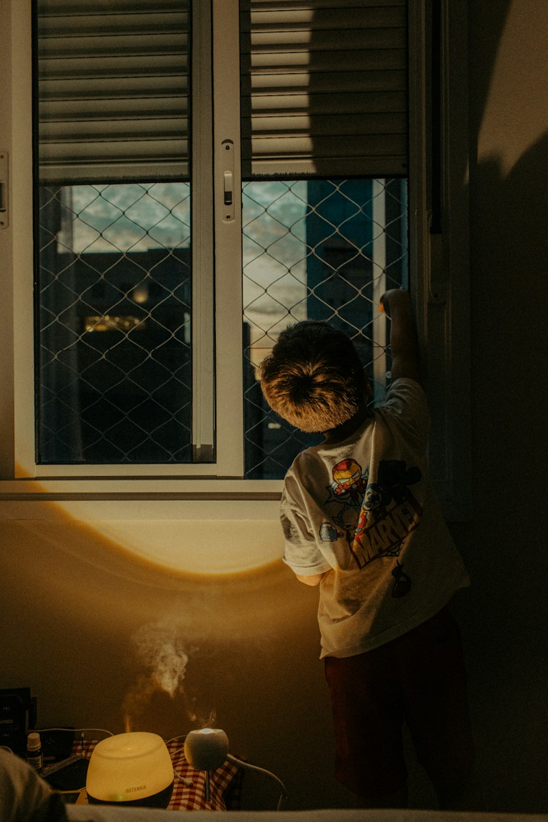 Child looking out a window at night with lamp light