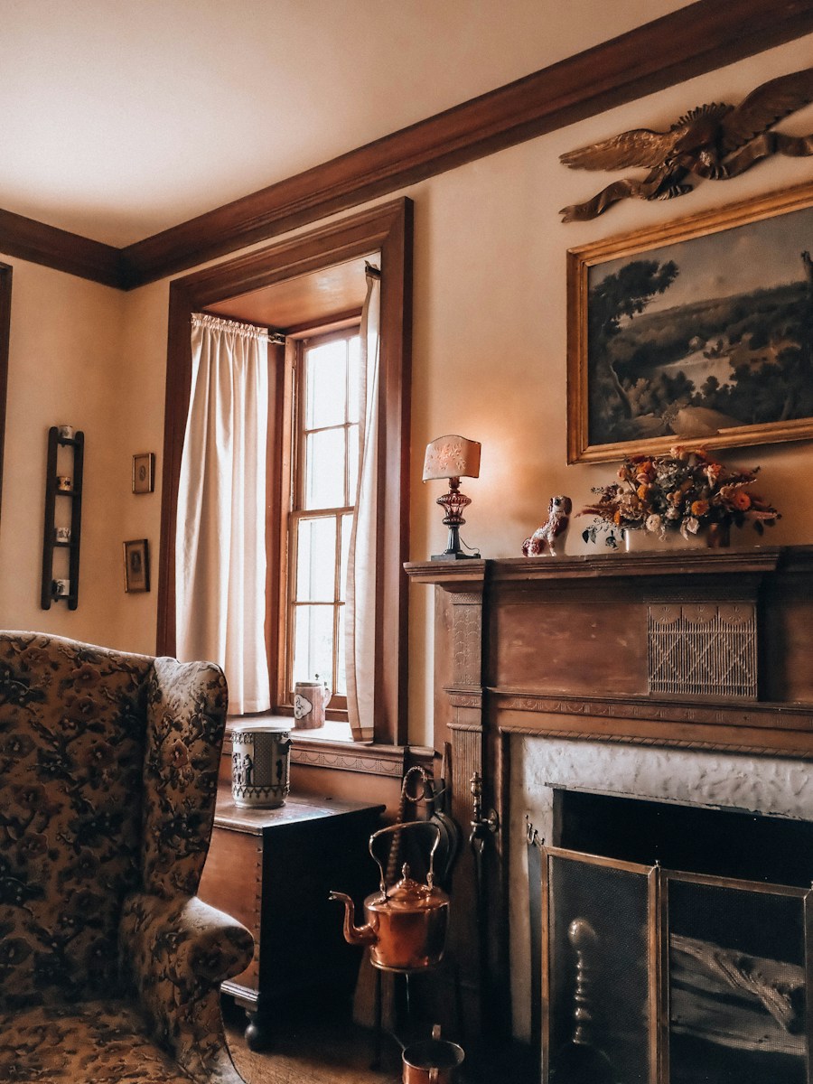 A cozy, antique room with a fireplace, window, and armchair
