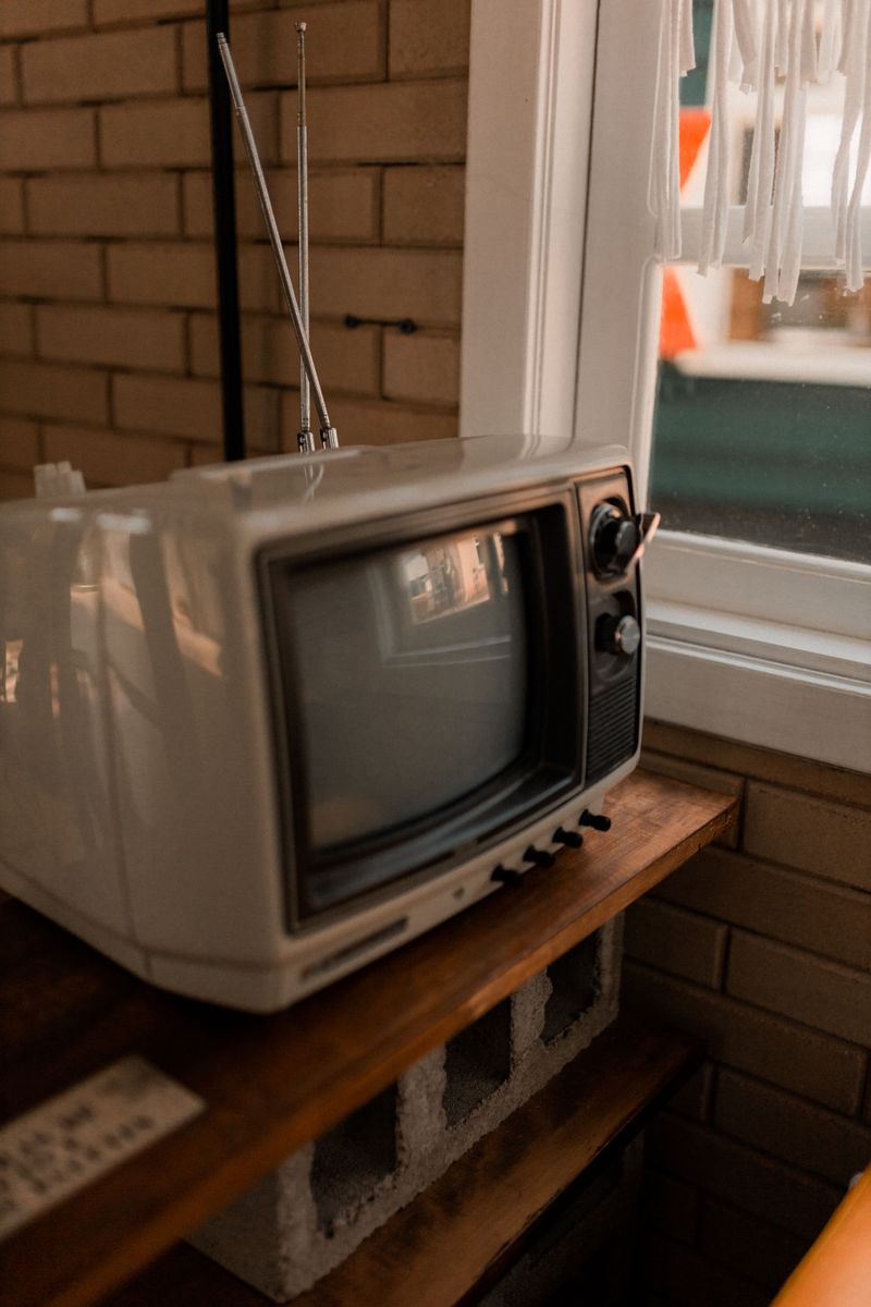 Vintage TV on a wooden shelf near a window in a cozy interior room.