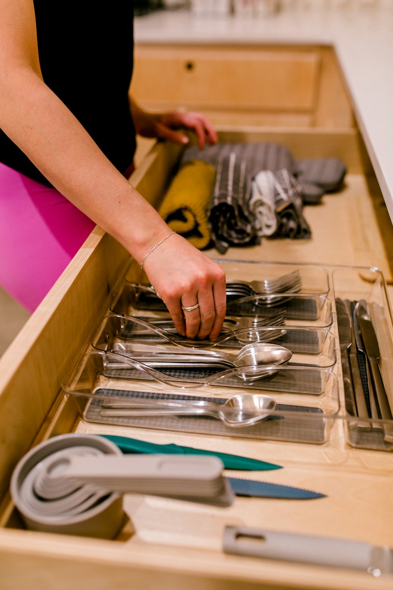 A hand organizing silverware in a kitchen drawer