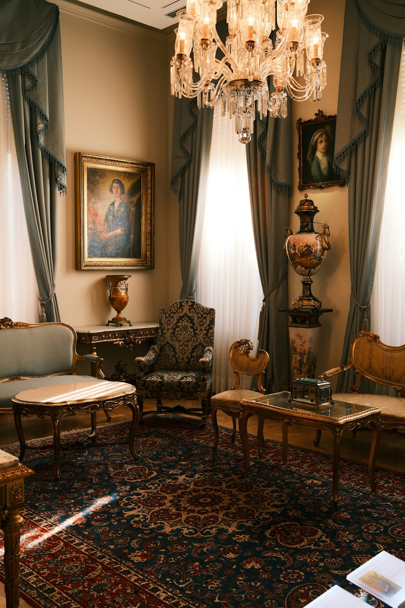 A formal living room with ornate furniture, a crystal chandelier, and oil paintings